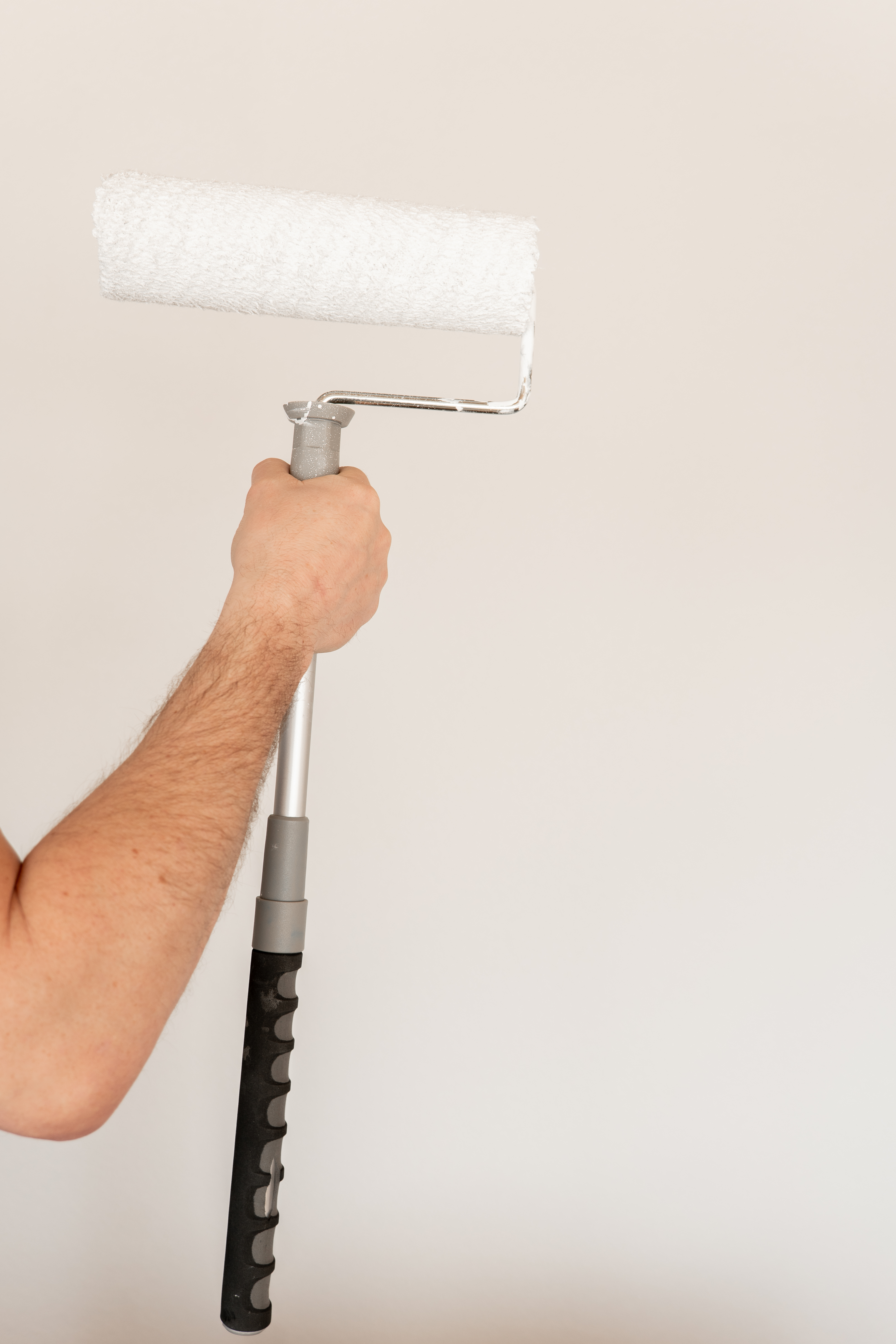 Holding Paint Roller on White Wall.Interior home renovation.A man paints a wall white with a paint roller.